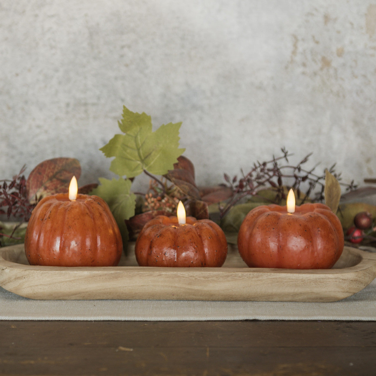 3 Flameless Pumpkin Candle shown in a wooden through bowl decorating a table for fall