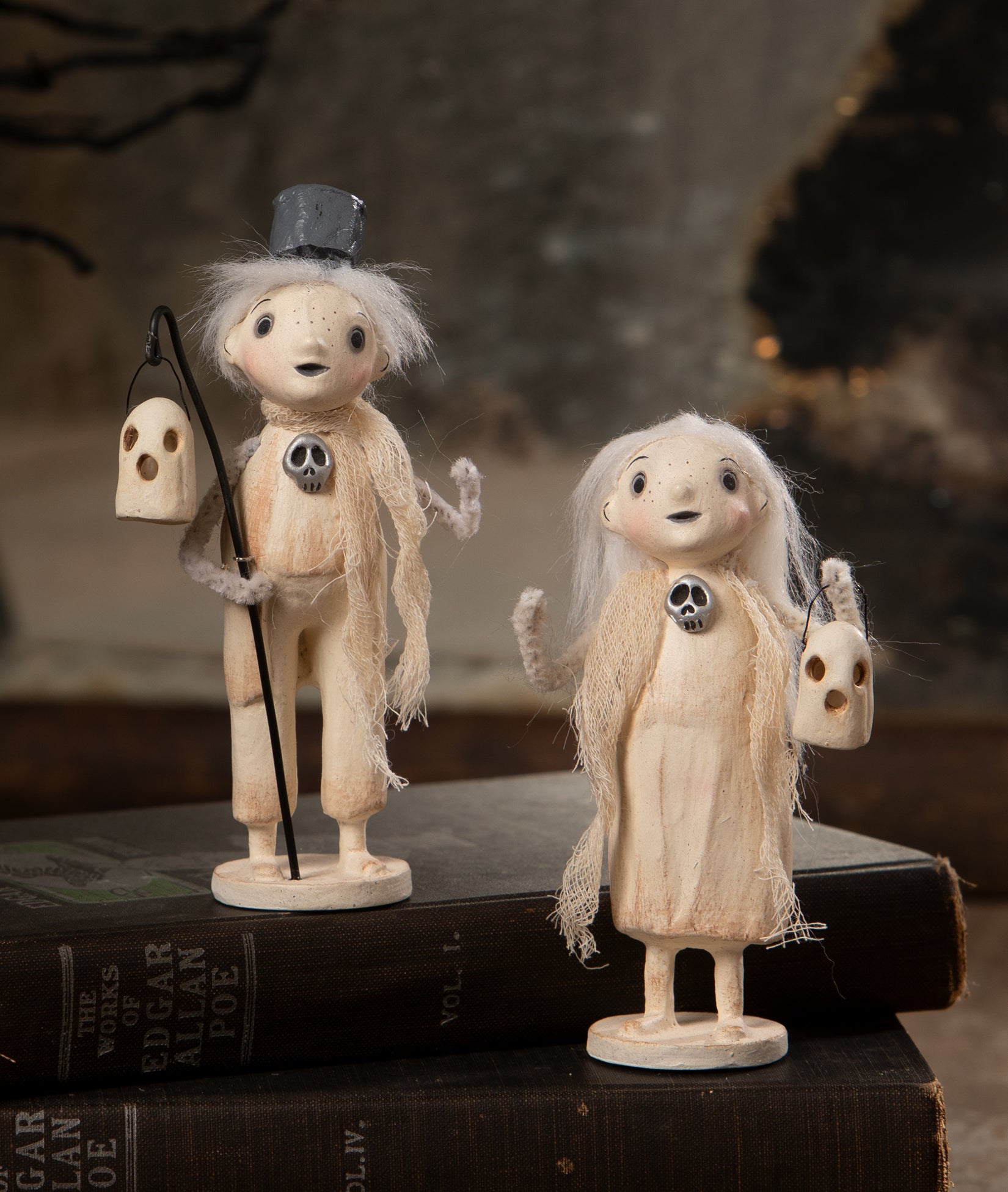 Two cute ghost figurines with ghost lanterns displayed on a book an Edgar Allan Poe book. Cute Halloween decorations designed by artist Michelle Lauritsen.