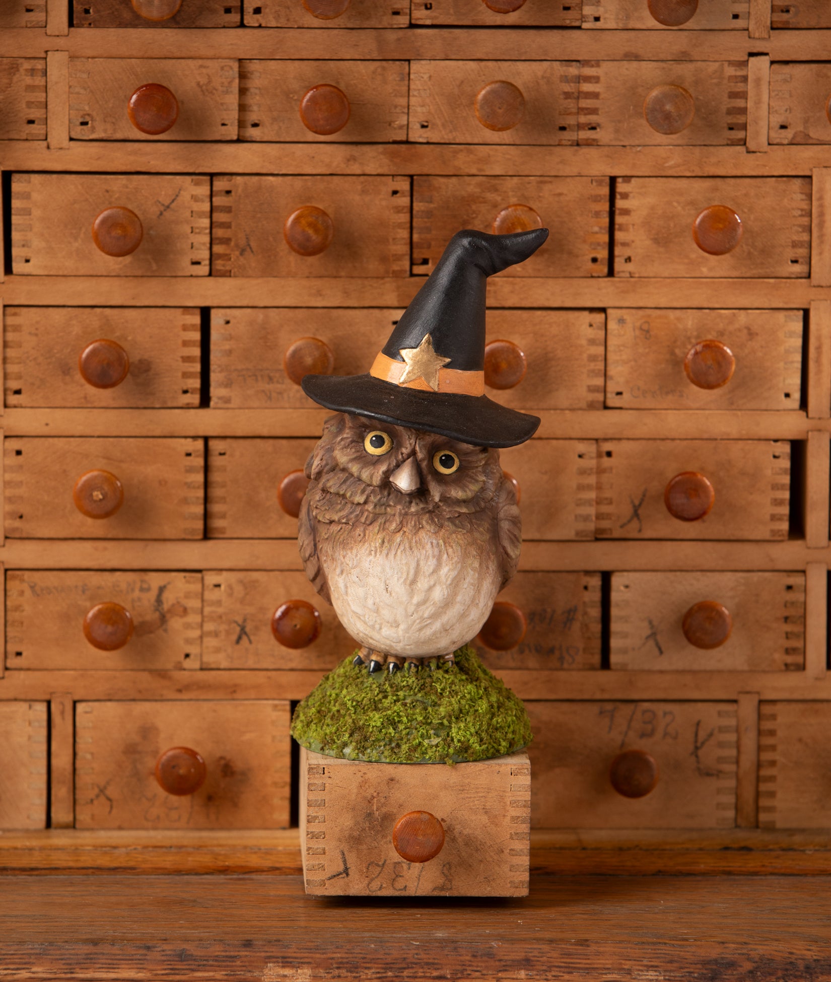 Owlina Witch - owl figurine wearing a witch hat on a wooden stand with a wooden drawer set background.