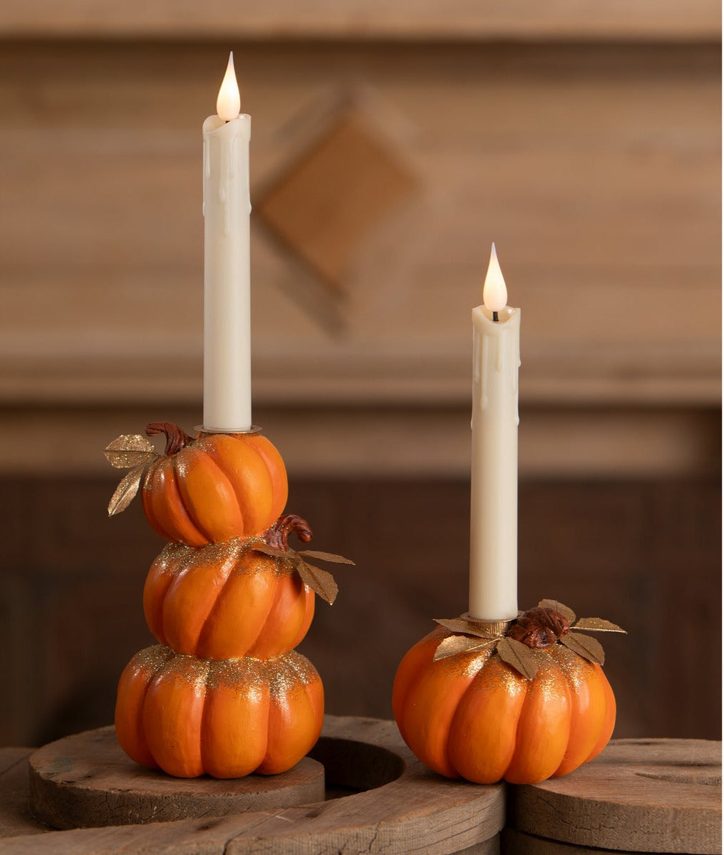 Stack of Pumpkins Candleholder and a single pumpkin candleholder with gold leaves and gold glitter shown with lit battery-operated taper candles on a wooden surface.
