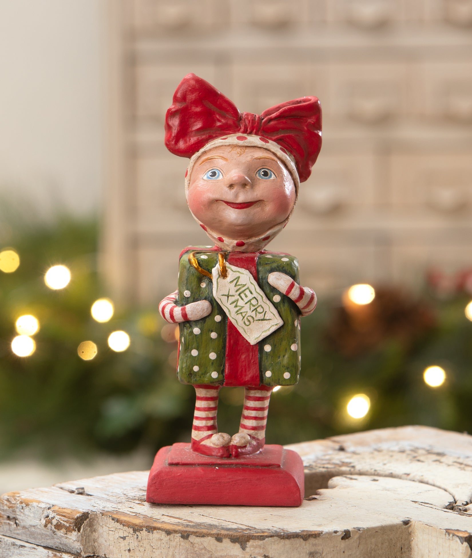 Surprise Package Girl figurine dressed up as a Christmas present with a big red bow on her head. Designed by Debra Schoch.